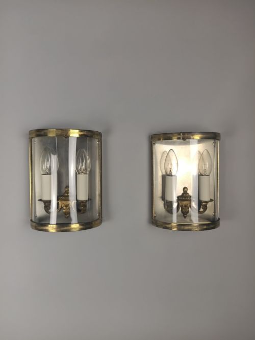 fig 2. A pair of French gilt brass half-lantern wall lights featuring curved clear glass panels and twin candle-style sockets.