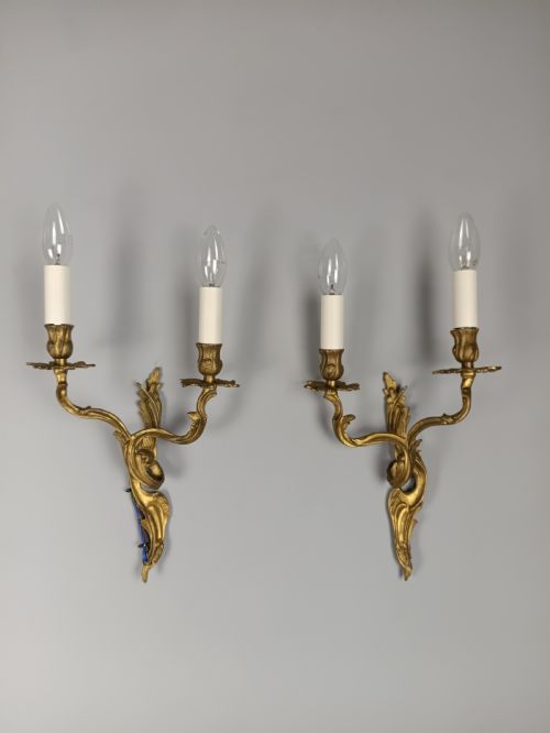 fig 3. A pair of two-arm gilded brass wall sconces featuring ornate Rococo scrolling leaf details and white candle-effect sleeves.