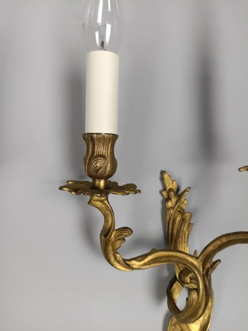 fig 5. A pair of two-arm gilded brass wall sconces featuring ornate Rococo scrolling leaf details and white candle-effect sleeves.