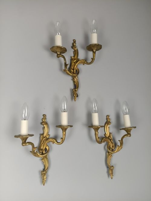fig 1. A set of three French gilded bronze twin-arm wall lights with ornate foliage scrolling and candle-style sockets.