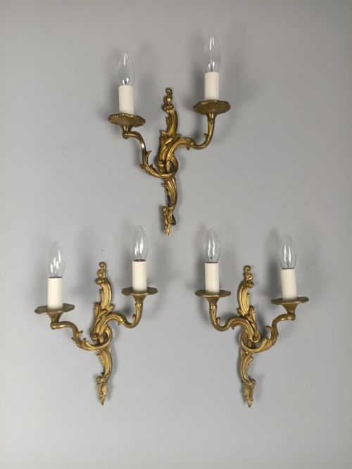 fig 5. A set of three French gilded bronze twin-arm wall lights with ornate foliage scrolling and candle-style sockets.