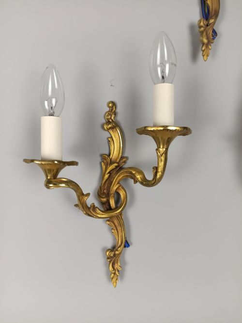 fig 2. Set of three French Rococo style gilt bronze wall sconces featuring twin sweeping arms, foliate scroll backplates, and candle-effect fittings.
