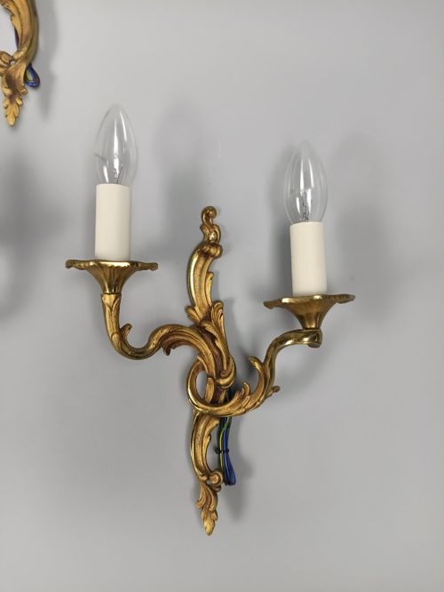 fig 3. Set of three French Rococo style gilt bronze wall sconces featuring twin sweeping arms, foliate scroll backplates, and candle-effect fittings.