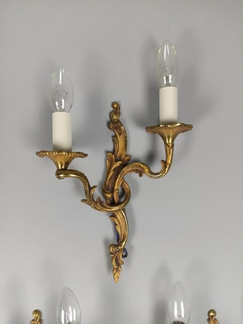 fig 4. Set of three French Rococo style gilt bronze wall sconces featuring twin sweeping arms, foliate scroll backplates, and candle-effect fittings.