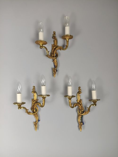 fig 5. Set of three French Rococo style gilt bronze wall sconces featuring twin sweeping arms, foliate scroll backplates, and candle-effect fittings.