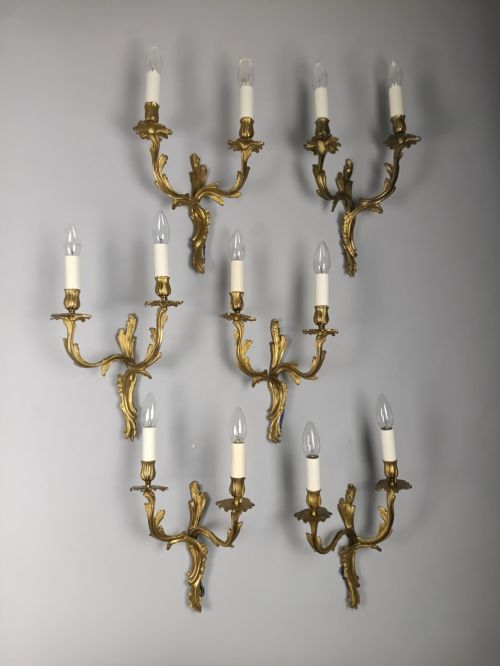 fig 1. A set of six French Rococo style twin-arm gilded brass wall lights featuring acanthus leaf scrollwork and white candle sleeves.