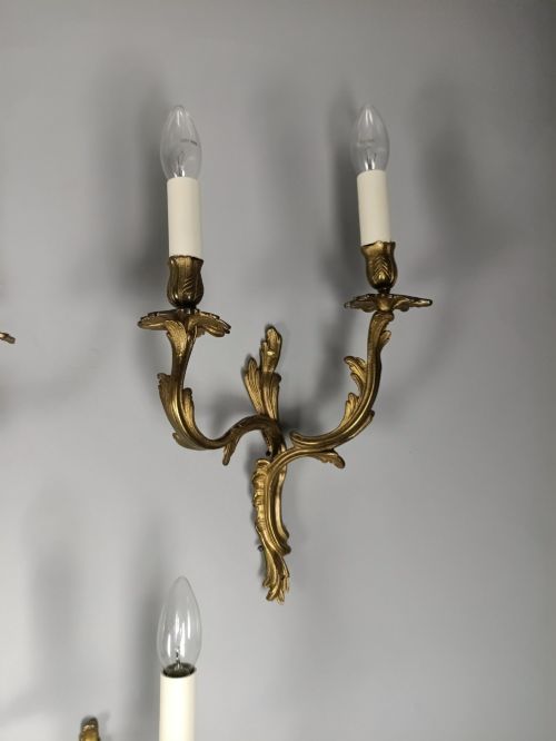 fig 3. A set of six French Rococo style twin-arm gilded brass wall lights featuring acanthus leaf scrollwork and white candle sleeves.