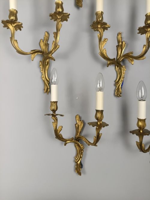 fig 6. A set of six French Rococo style twin-arm gilded brass wall lights featuring acanthus leaf scrollwork and white candle sleeves.