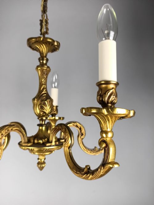 fig 2. A five-arm French gilt bronze chandelier featuring acanthus leaf scroll arms, candle-style sockets, and an ornate central column suspended by a chain.