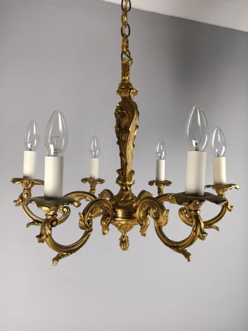 fig 1. A French six-light gilt bronze chandelier featuring scrolling acanthus leaf arms, candle-style bulb sleeves, and an ornamental central stem suspended from a chain.