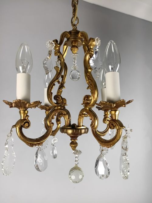 fig 1. A four-arm French gilt metal chandelier decorated with scrolling arms, candle-style light sockets, and hanging faceted cut crystal drops.