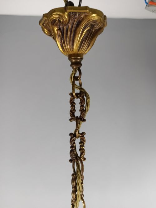 fig 2. A four-arm French gilt metal chandelier decorated with scrolling arms, candle-style light sockets, and hanging faceted cut crystal drops.