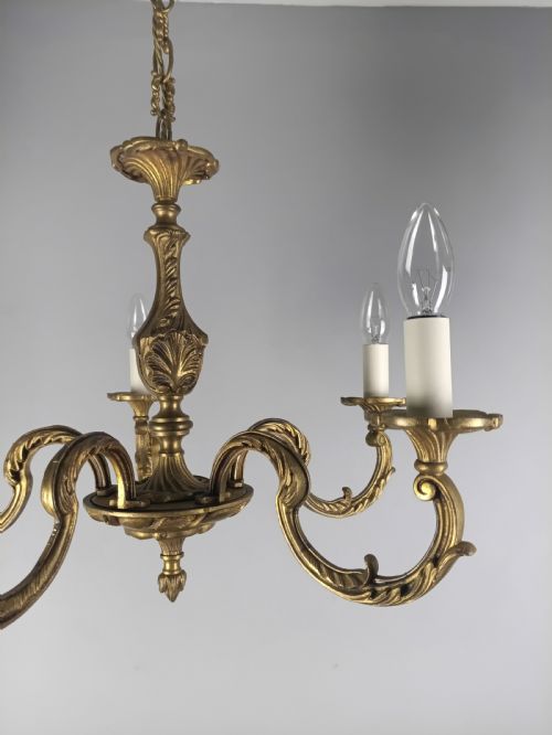 fig 1. A French gilt brass five-arm chandelier featuring ornate scrolled branches, leaf motifs, and candle bulb sockets suspended from a central chain.