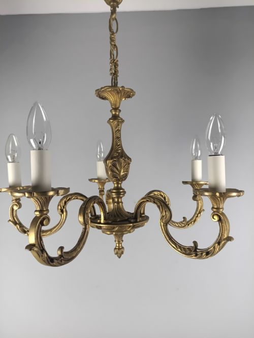 fig 2. A French gilt brass five-arm chandelier featuring ornate scrolled branches, leaf motifs, and candle bulb sockets suspended from a central chain.