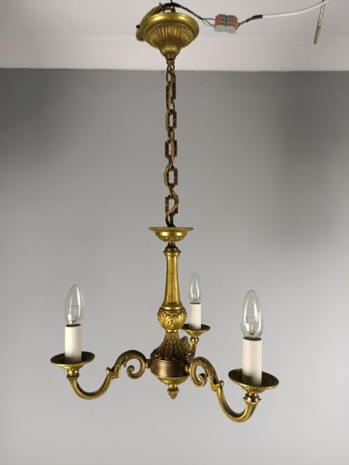 fig 2. A three-arm gilt brass ceiling chandelier featuring scrolled branches, acanthus leaf decoration, and a central tapered column suspended by a chain.