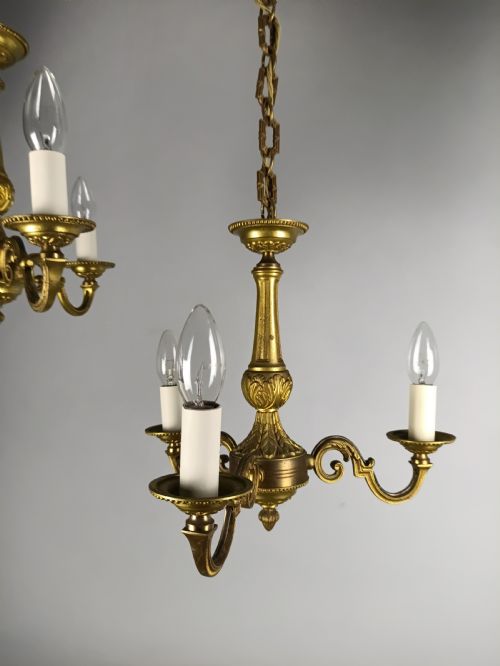 fig 1. A pair of French gilt brass three-arm chandeliers featuring scrolling branches and fluted central columns suspended from metal chains.