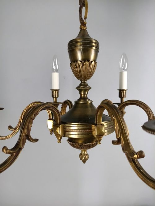 fig 1. A French antique-style bronze six-arm chandelier featuring scrolling candle arms, white candle sleeves, and a central urn-shaped stem suspended from a metal chain.