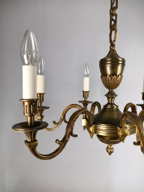 fig 2. A French antique-style bronze six-arm chandelier featuring scrolling candle arms, white candle sleeves, and a central urn-shaped stem suspended from a metal chain.