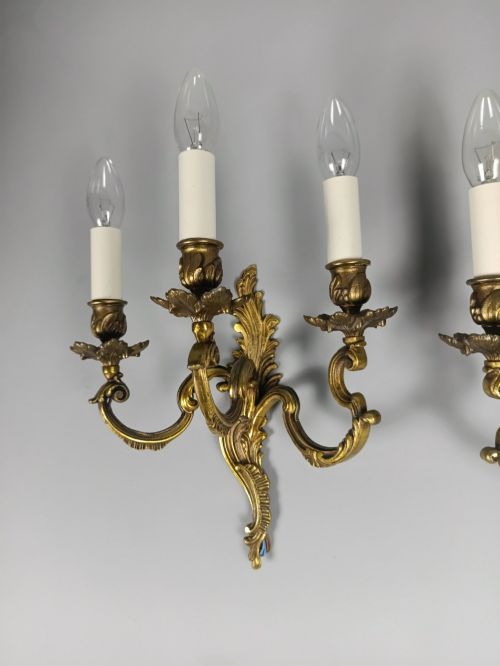 fig 3. A pair of French Rococo style triple-arm gilded bronze wall lights featuring ornate foliage scrollwork and white candle sleeves.