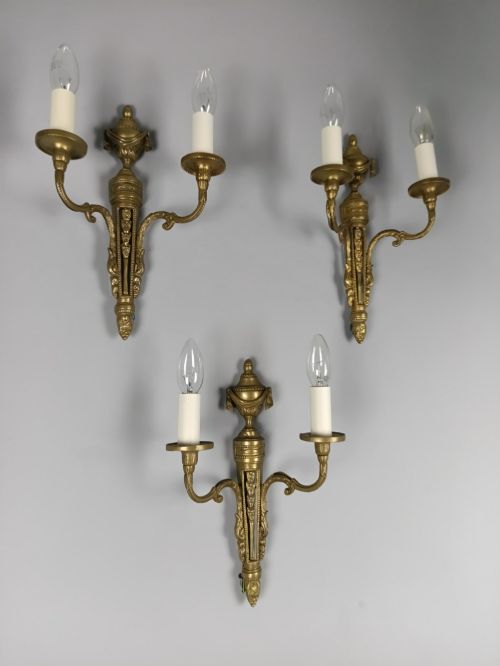 fig 1. A set of three French Neoclassical gilt brass twin-arm wall sconces featuring urn finials and decorative candle branches.