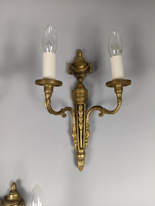 fig 3. A set of three French Neoclassical gilt brass twin-arm wall sconces featuring urn finials and decorative candle branches.