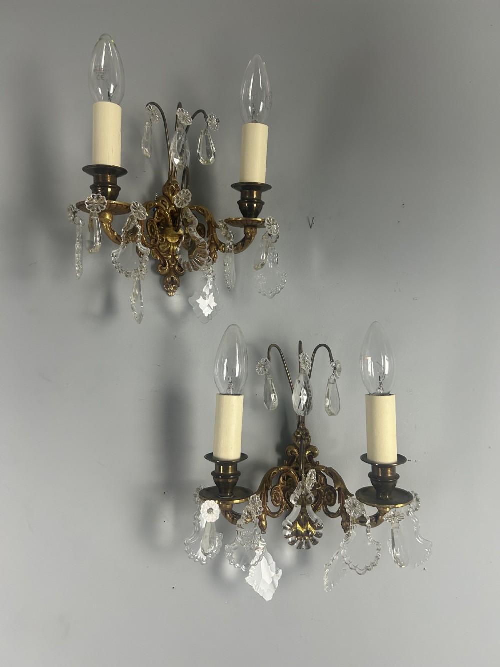 A pair of French gilt brass twin-arm wall lights decorated with scrollwork and hanging crystal drops.