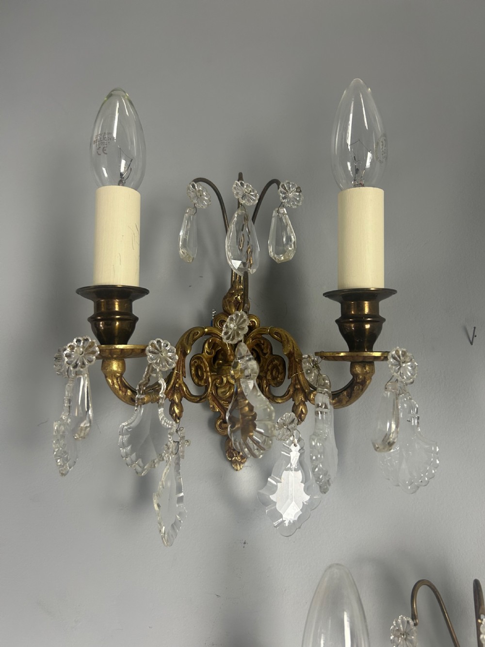 A pair of French gilt brass twin-arm wall lights decorated with scrollwork and hanging crystal drops. View II