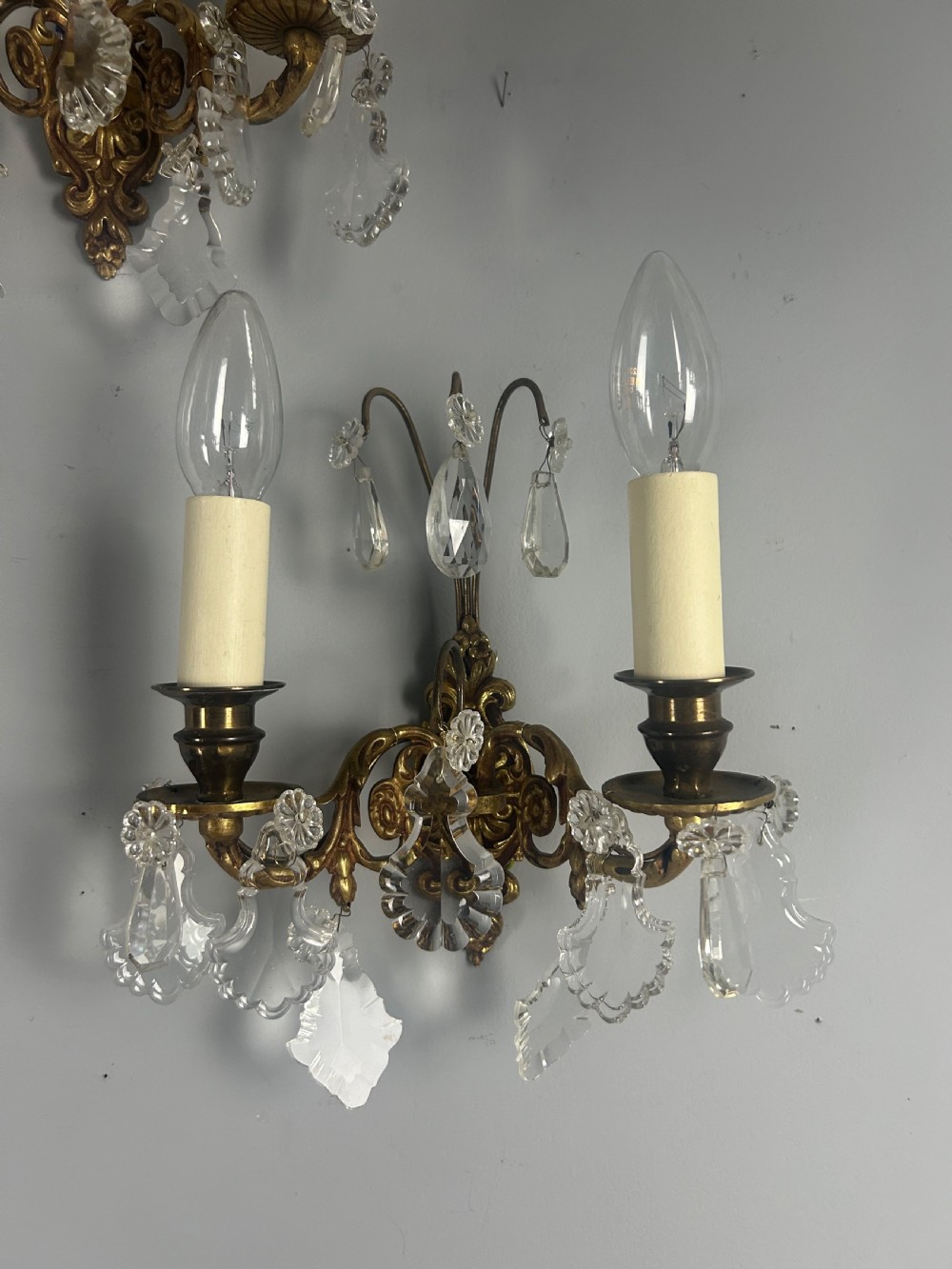 A pair of French gilt brass twin-arm wall lights decorated with scrollwork and hanging crystal drops. View III