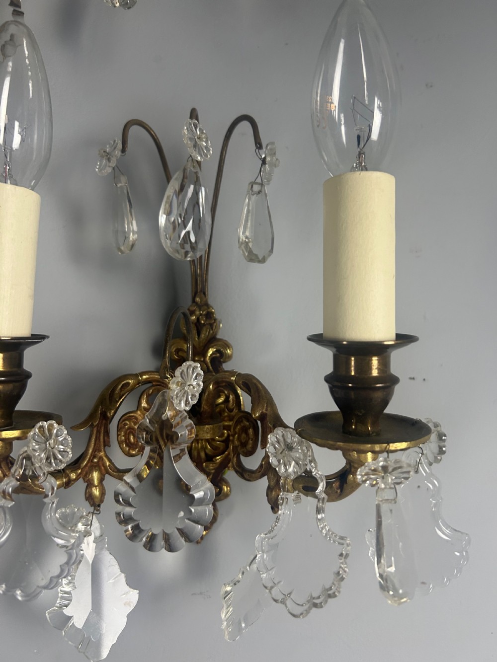 A pair of French gilt brass twin-arm wall lights decorated with scrollwork and hanging crystal drops. View IV