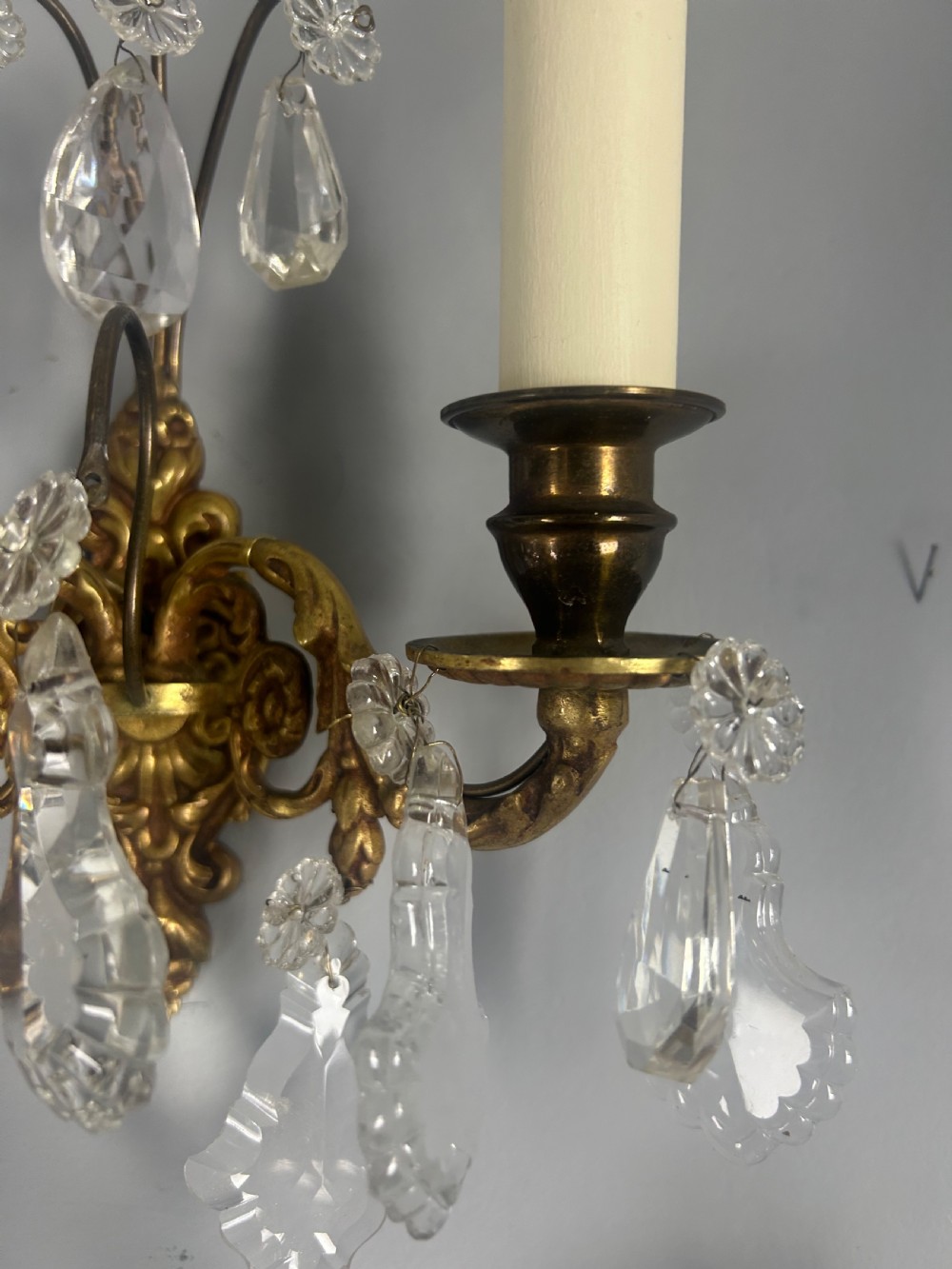 A pair of French gilt brass twin-arm wall lights decorated with scrollwork and hanging crystal drops. View V