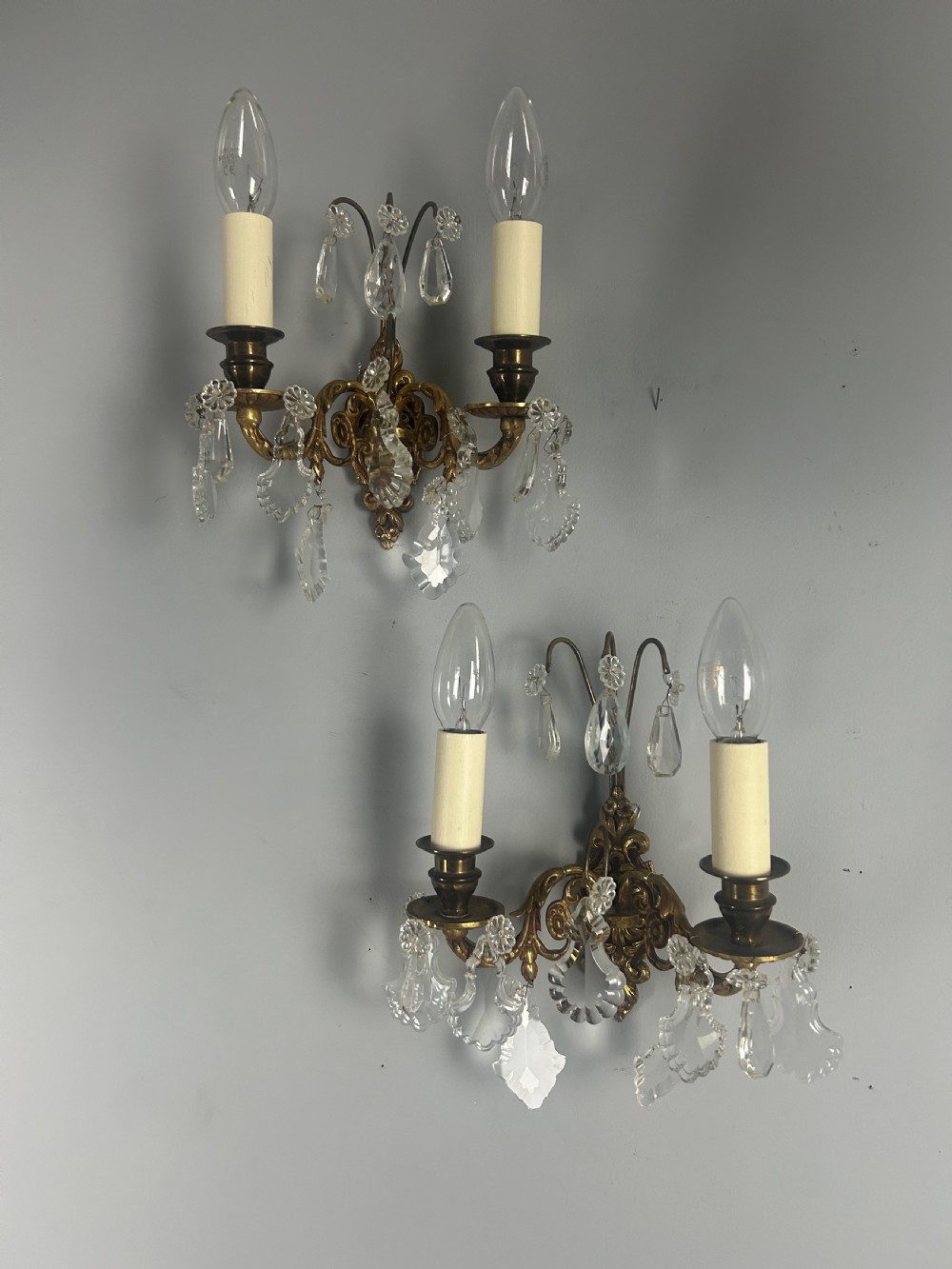 A pair of French gilt brass twin-arm wall lights decorated with scrollwork and hanging crystal drops. View VII