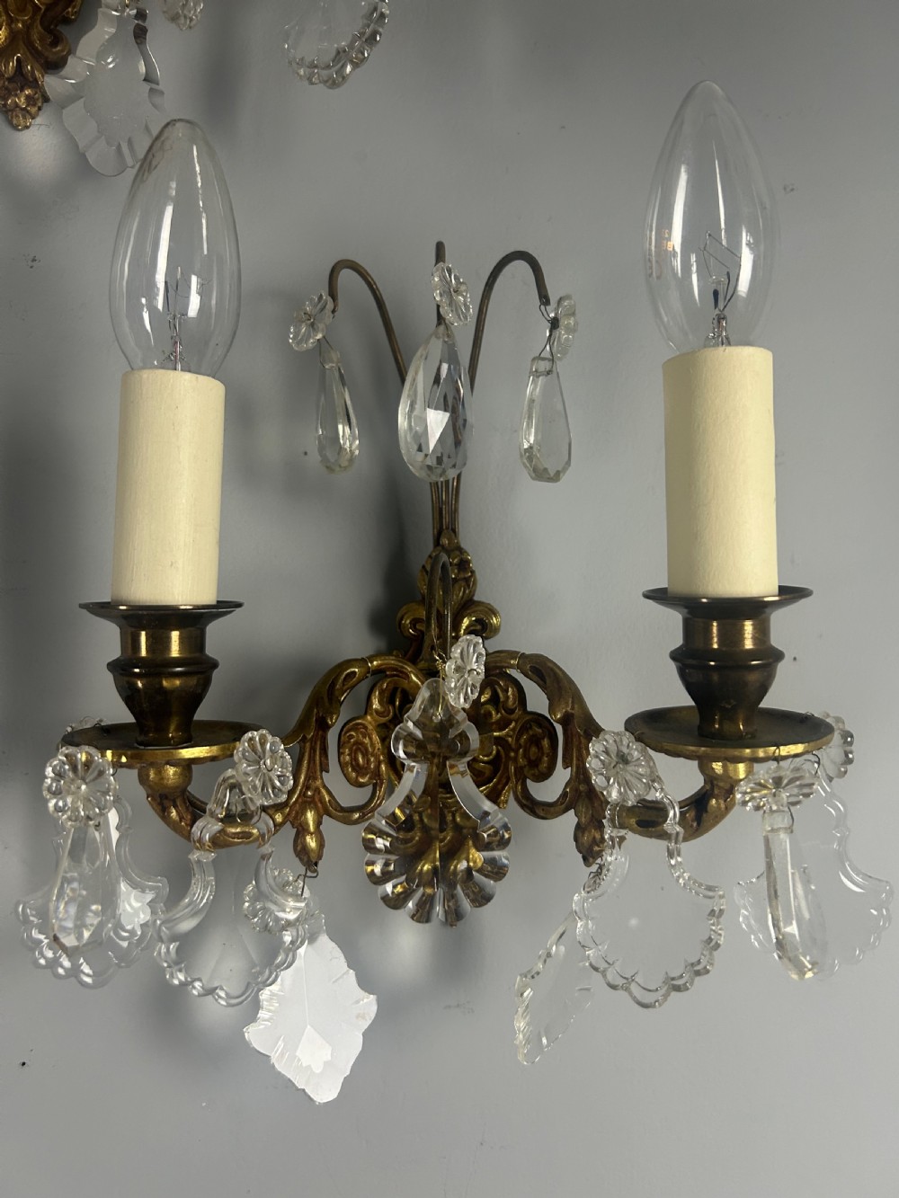 A pair of French gilt brass twin-arm wall lights decorated with scrollwork and hanging crystal drops. View VIII