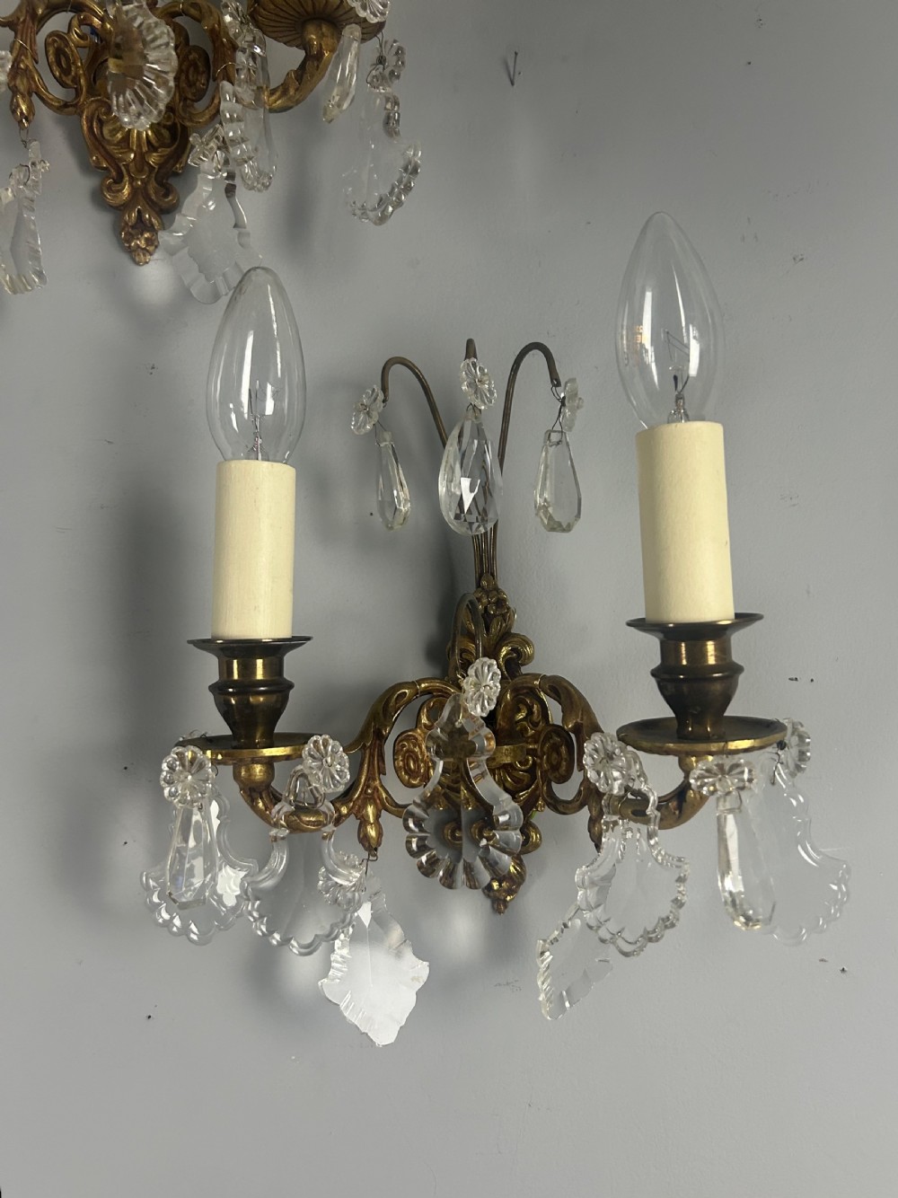 A pair of French gilt brass twin-arm wall lights decorated with scrollwork and hanging crystal drops. View IX