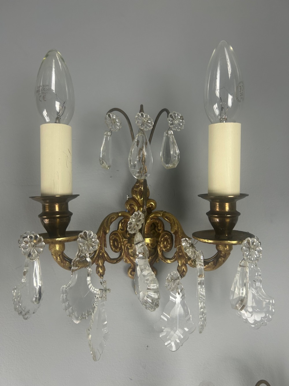 A pair of French gilt brass twin-arm wall lights decorated with scrollwork and hanging crystal drops. View XI