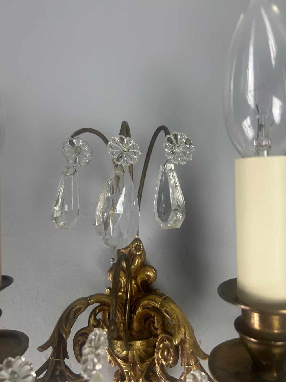 A pair of French gilt brass twin-arm wall lights decorated with scrollwork and hanging crystal drops. View XII