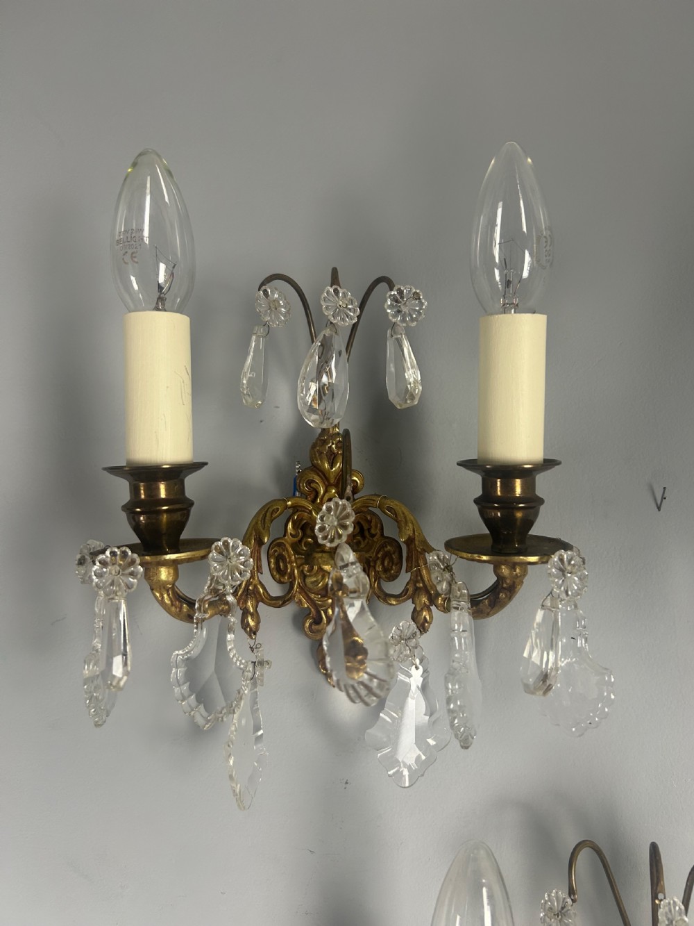 A pair of French gilt brass twin-arm wall lights decorated with scrollwork and hanging crystal drops. View XIII
