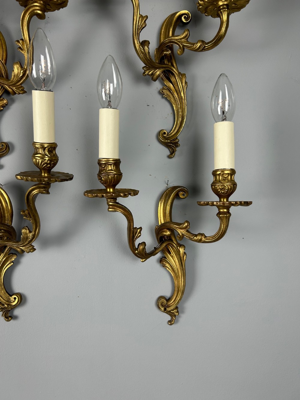 A set of four antique French twin-arm wall lights with a gilded finish and candle-style bulbs. View III
