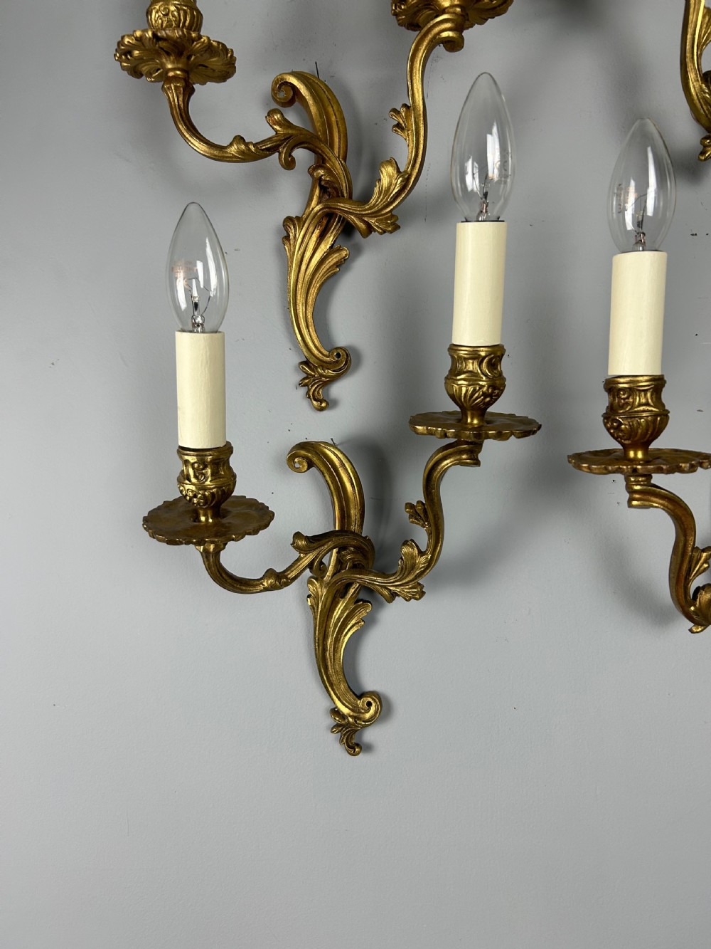 A set of four antique French twin-arm wall lights with a gilded finish and candle-style bulbs. View V