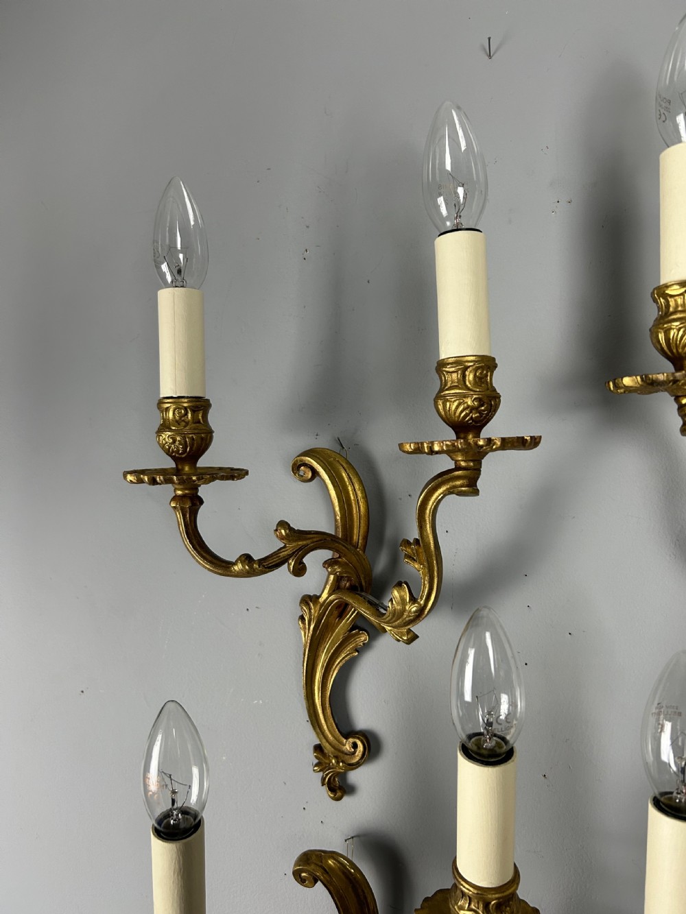 A set of four antique French twin-arm wall lights with a gilded finish and candle-style bulbs. View VI