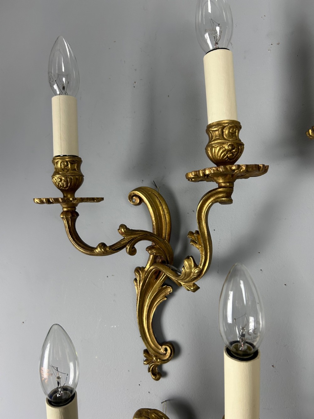 A set of four antique French twin-arm wall lights with a gilded finish and candle-style bulbs. View VII