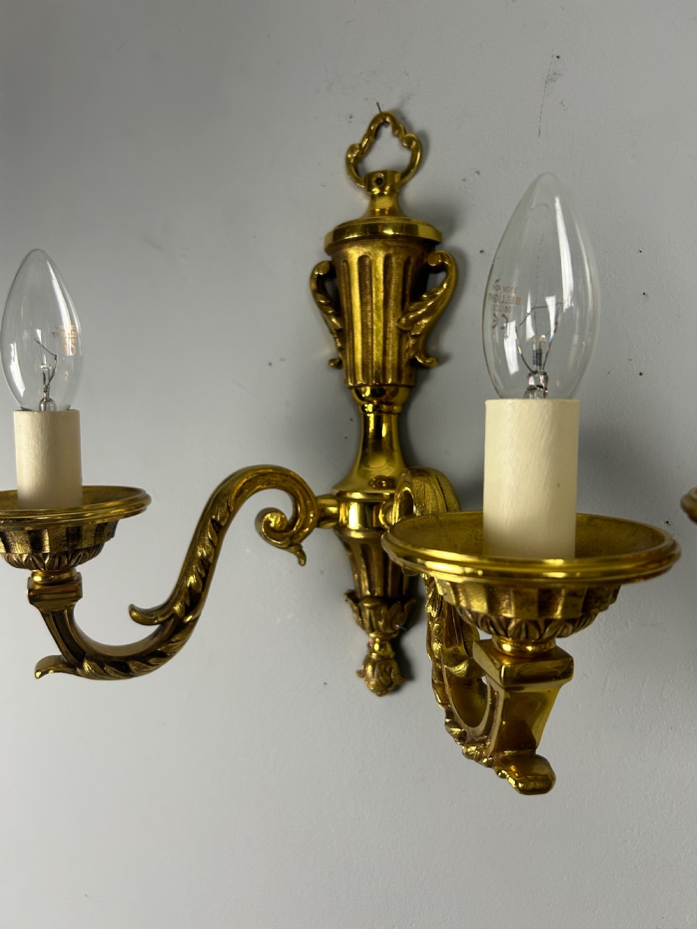 A pair of ornate French gilt brass wall lights featuring twin scrolling arms and central urn motifs against a neutral background. View II