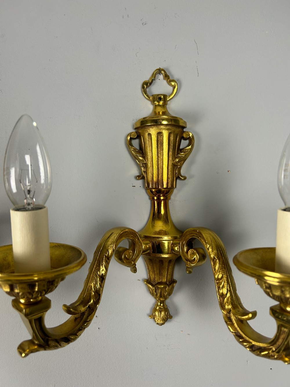 A pair of ornate French gilt brass wall lights featuring twin scrolling arms and central urn motifs against a neutral background. View III