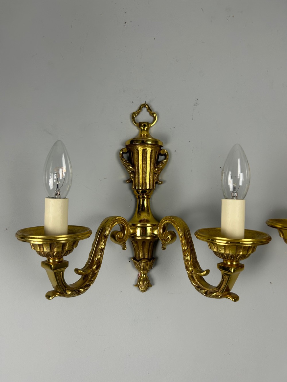 A pair of ornate French gilt brass wall lights featuring twin scrolling arms and central urn motifs against a neutral background. View VI