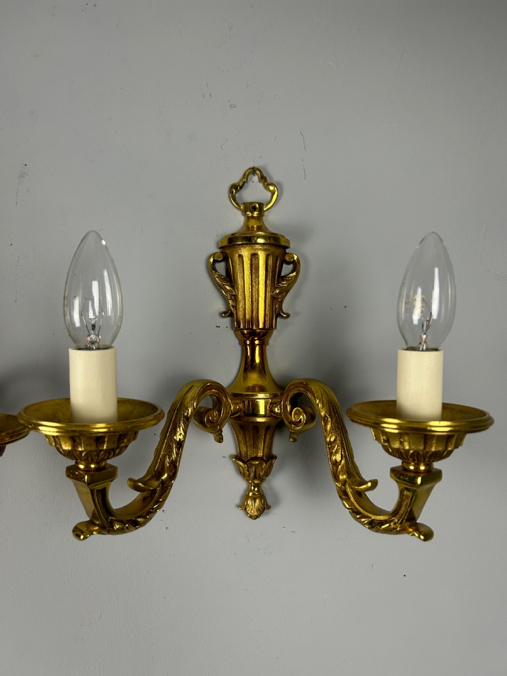 A pair of ornate French gilt brass wall lights featuring twin scrolling arms and central urn motifs against a neutral background. View VIII