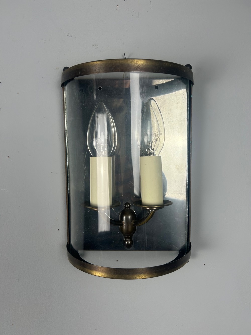 A half-cylinder brass wall light featuring curved glass panels and two candle-style bulbs.