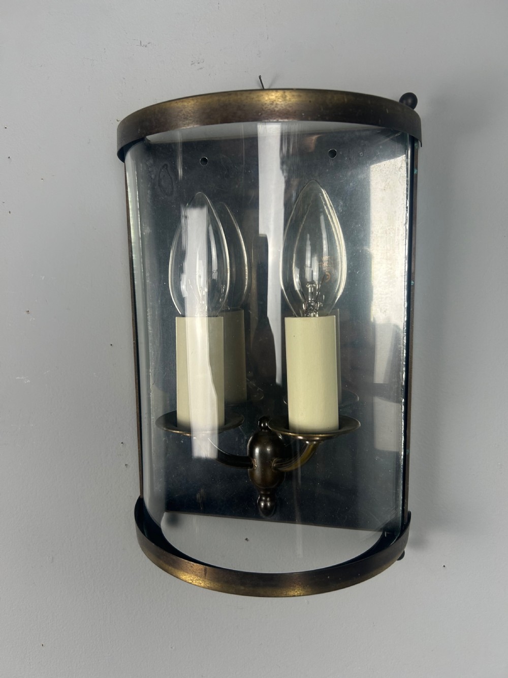 A half-cylinder brass wall light featuring curved glass panels and two candle-style bulbs. View IV