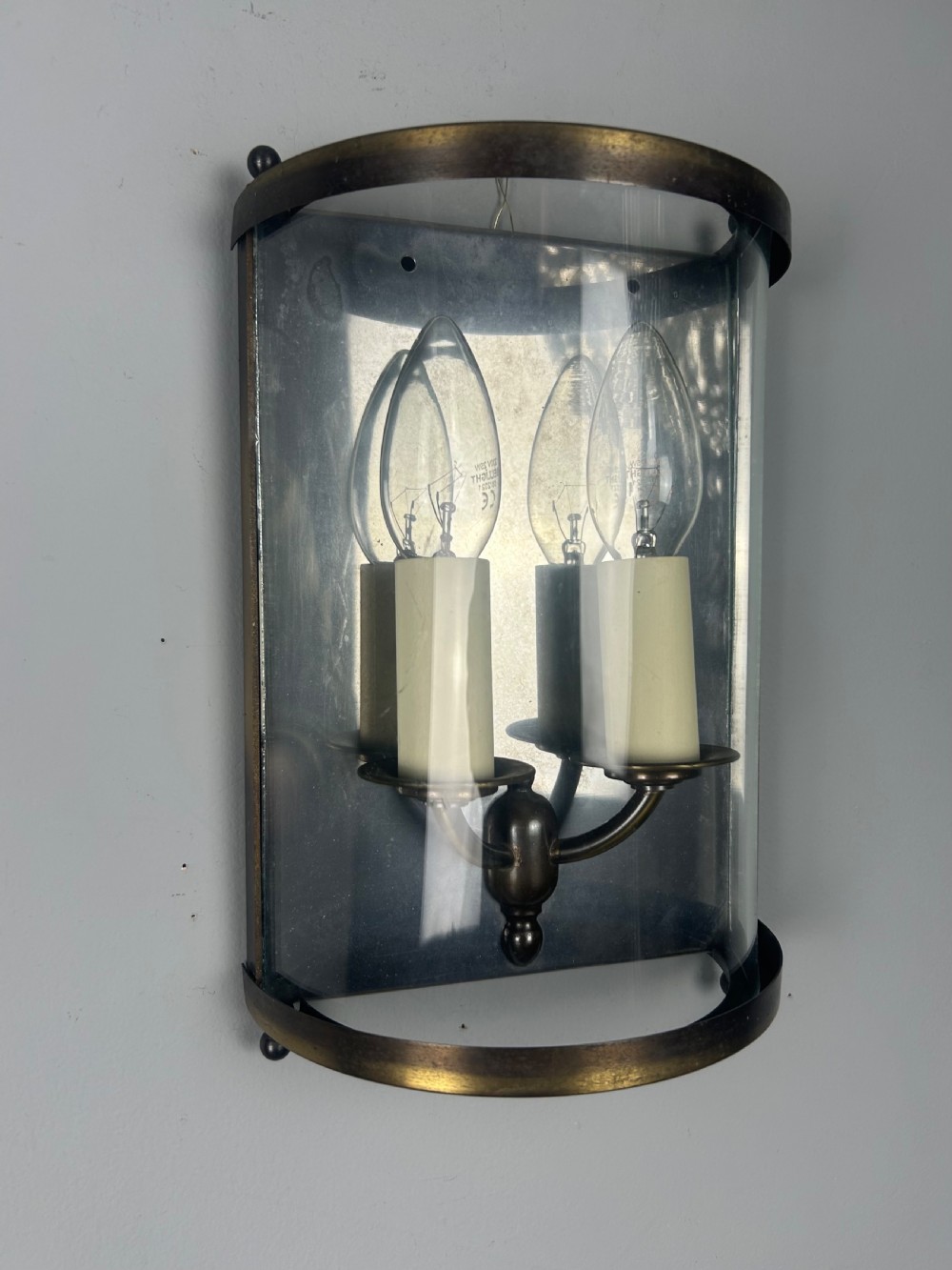 A half-cylinder brass wall light featuring curved glass panels and two candle-style bulbs. View V