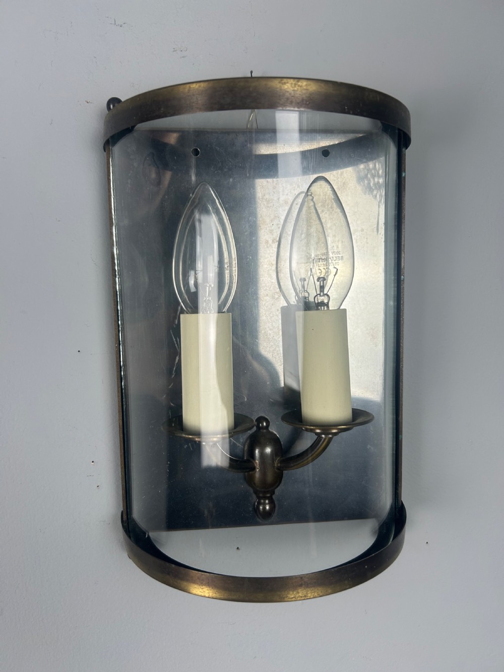 A half-cylinder brass wall light featuring curved glass panels and two candle-style bulbs. View VI