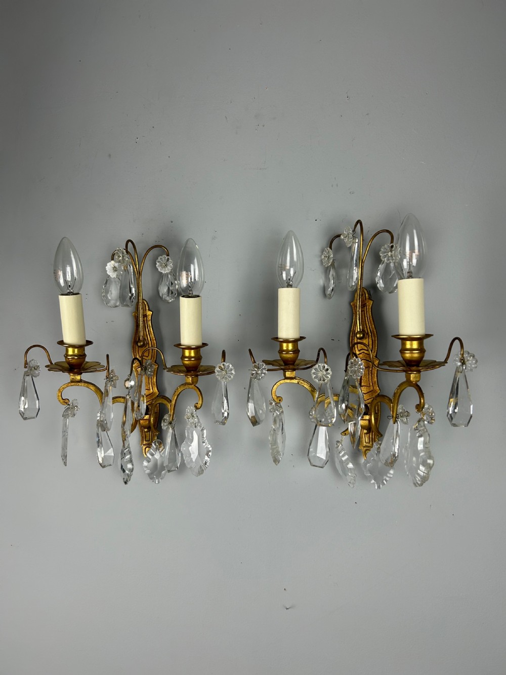 A pair of antique twin-arm wall lights featuring gilded frames and cascading crystal drops against a neutral background. View III