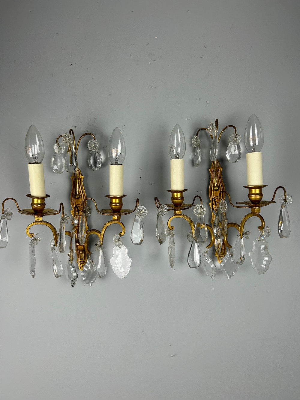 A pair of antique twin-arm wall lights featuring gilded frames and cascading crystal drops against a neutral background. View IV